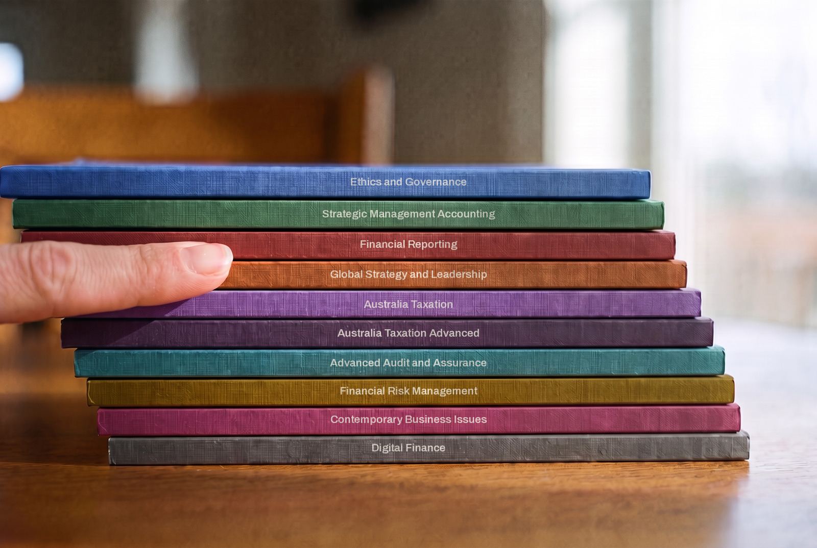 Ten study packs stacked on a table, each in its own colour with its subject name printed along the edge, a fingertip resting on the stack