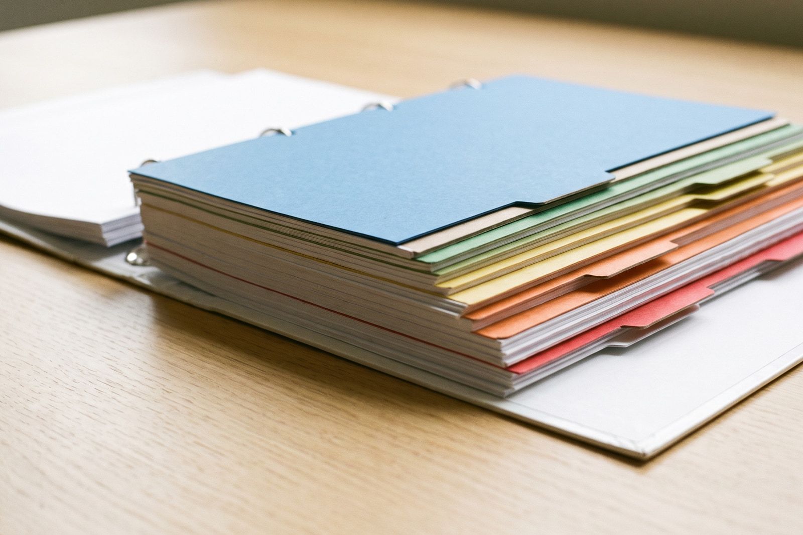 A ring binder open on a pale oak desk, its coloured index tabs standing off the page block.